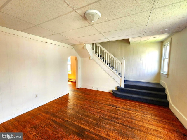 interior space with a baseboard heating unit, wood-type flooring, wooden walls, and a paneled ceiling