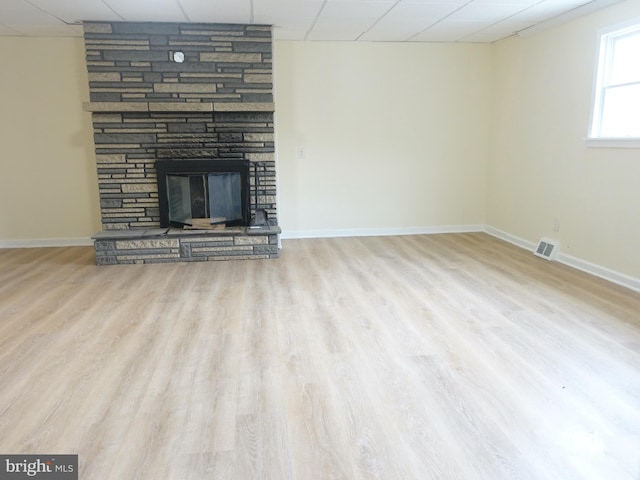 unfurnished living room featuring a paneled ceiling, a stone fireplace, and hardwood / wood-style floors