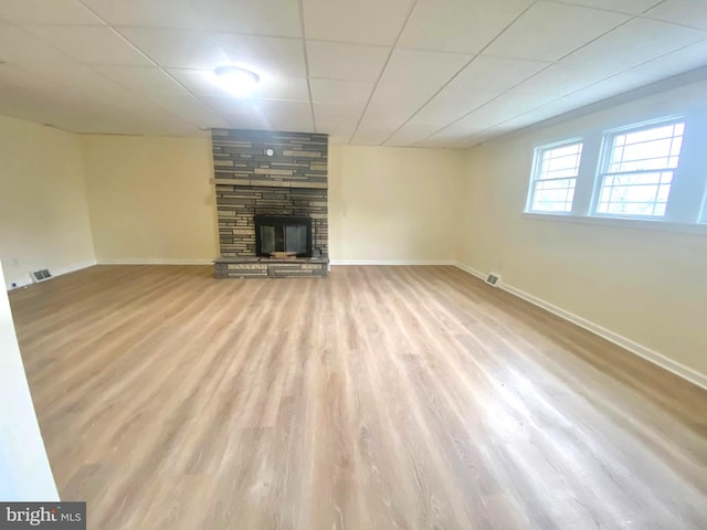 unfurnished living room with a drop ceiling, light wood-type flooring, and a fireplace