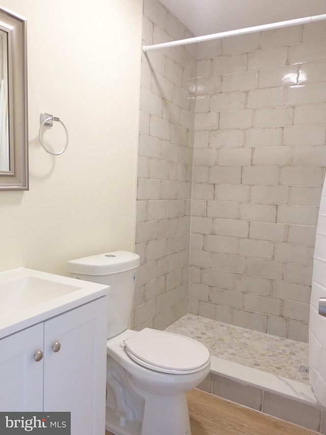 bathroom featuring a tile shower, vanity, wood-type flooring, and toilet