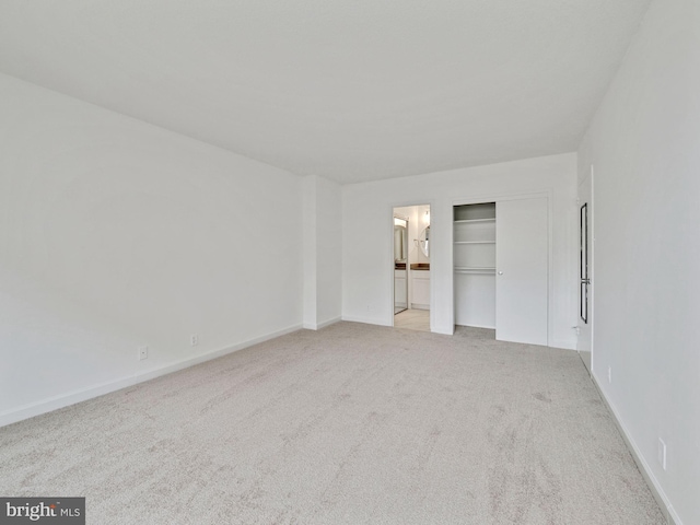 unfurnished bedroom with a closet, light colored carpet, and ensuite bath