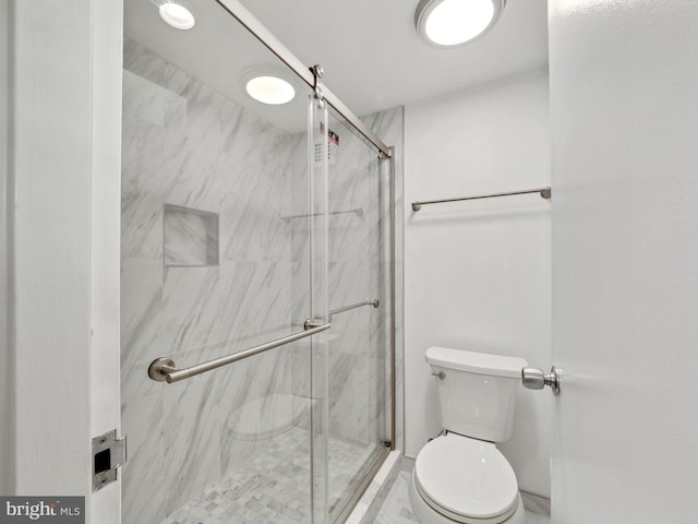 bathroom featuring a shower with door and toilet