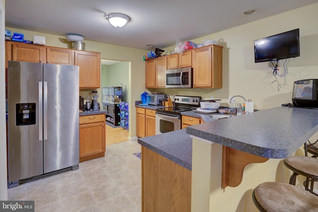 kitchen with kitchen peninsula, light tile flooring, sink, a breakfast bar area, and appliances with stainless steel finishes