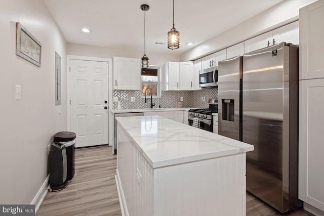 kitchen with light stone countertops, pendant lighting, white cabinets, a center island, and stainless steel appliances