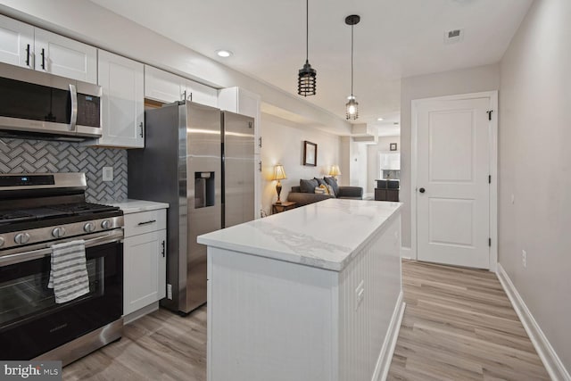 kitchen with appliances with stainless steel finishes, a center island, white cabinetry, decorative backsplash, and hanging light fixtures