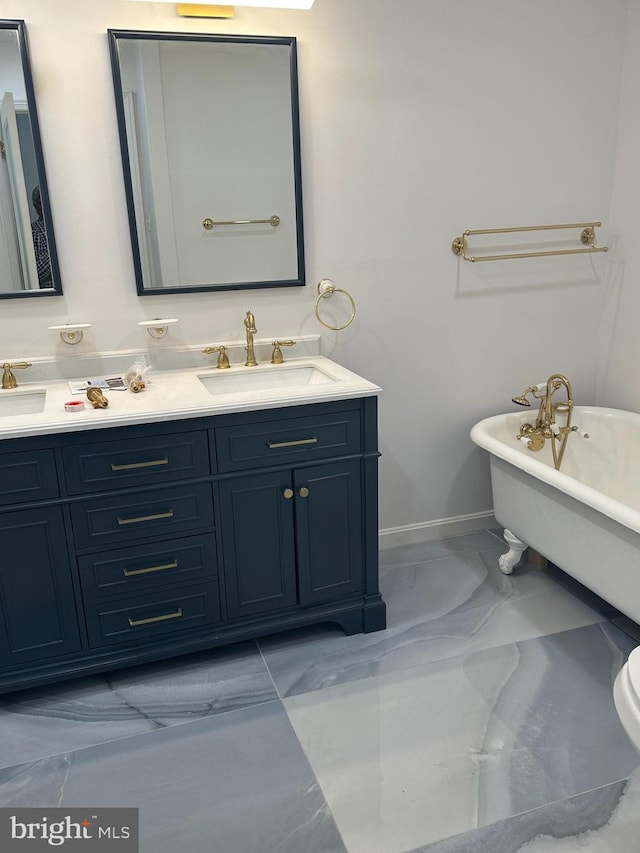 bathroom with double vanity, marble finish floor, a freestanding tub, and a sink