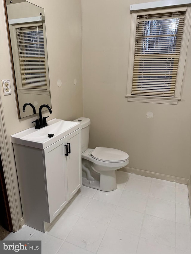 half bath featuring tile patterned flooring, vanity, toilet, and baseboards