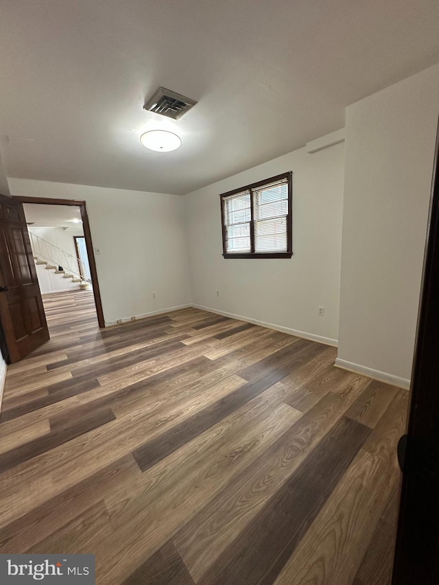 empty room featuring stairway, wood finished floors, visible vents, and baseboards