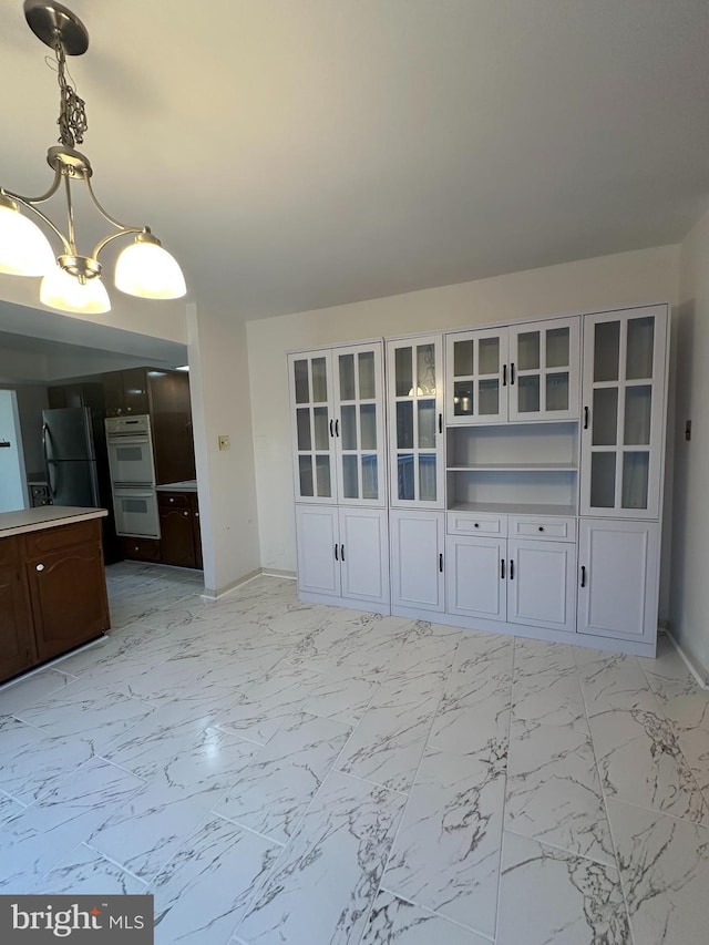 unfurnished dining area featuring marble finish floor, an inviting chandelier, and baseboards