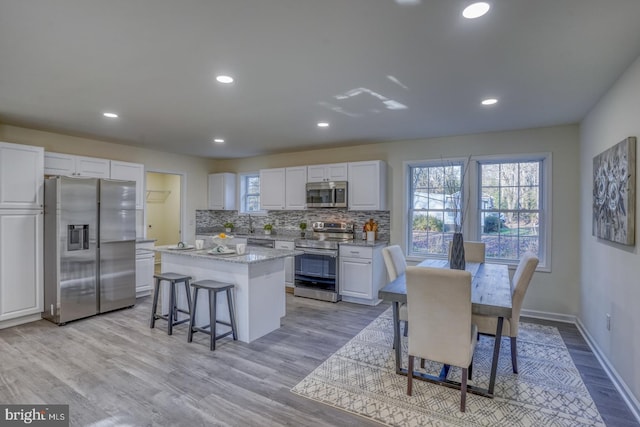 kitchen featuring light hardwood / wood-style floors, a kitchen island, backsplash, white cabinetry, and appliances with stainless steel finishes