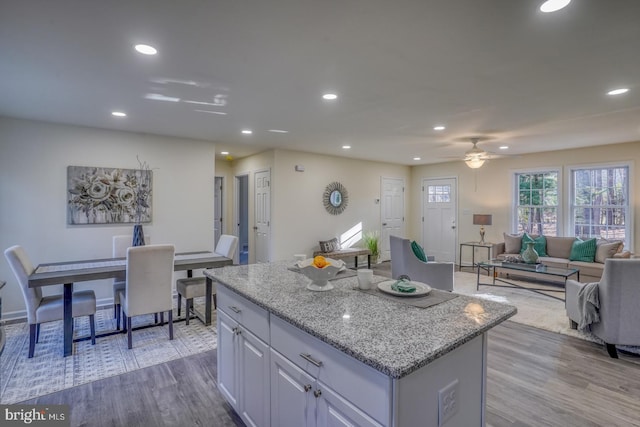 kitchen with a center island, white cabinetry, light stone countertops, light hardwood / wood-style flooring, and ceiling fan