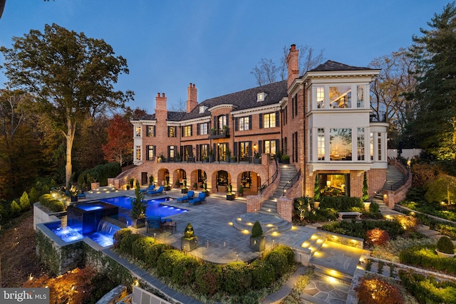 back house at dusk featuring pool water feature, a patio, and an in ground hot tub