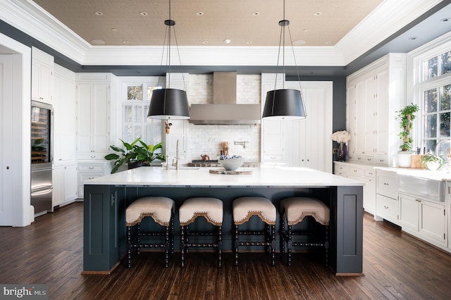 kitchen with wall chimney exhaust hood, dark wood-type flooring, a spacious island, decorative light fixtures, and white cabinets