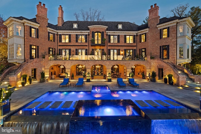 back house at dusk with a swimming pool with hot tub, pool water feature, and a patio area