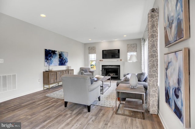 living room featuring a glass covered fireplace, visible vents, baseboards, and wood finished floors