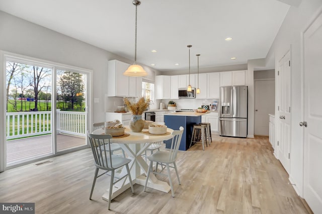 kitchen featuring a kitchen island, white cabinetry, light countertops, appliances with stainless steel finishes, and decorative light fixtures