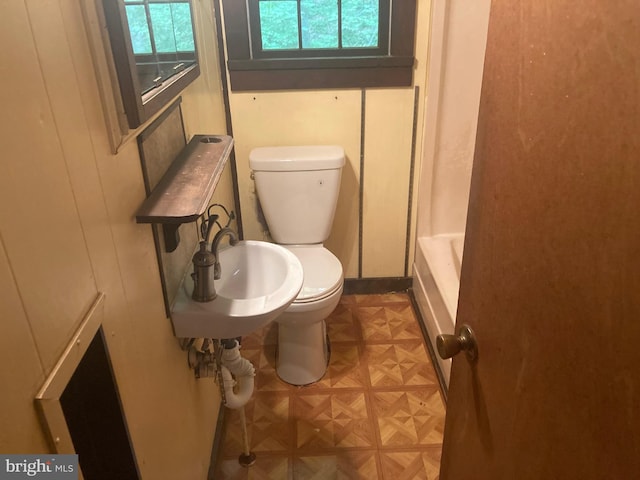 bathroom featuring a tub to relax in, parquet floors, toilet, and a healthy amount of sunlight