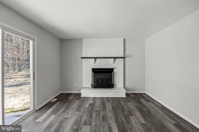 unfurnished living room with a brick fireplace, brick wall, and dark wood-type flooring