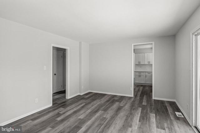 unfurnished bedroom with ensuite bath, a closet, a walk in closet, and dark wood-type flooring