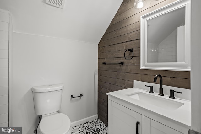 bathroom with tile floors, wood walls, lofted ceiling, toilet, and large vanity