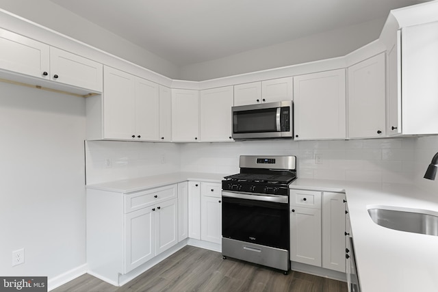 kitchen featuring stainless steel appliances, white cabinets, dark hardwood / wood-style floors, backsplash, and sink