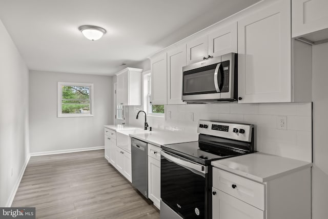 kitchen with tasteful backsplash, stainless steel appliances, light wood-type flooring, sink, and white cabinetry