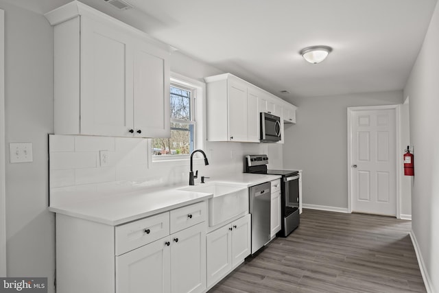 kitchen with tasteful backsplash, wood-type flooring, sink, white cabinetry, and appliances with stainless steel finishes