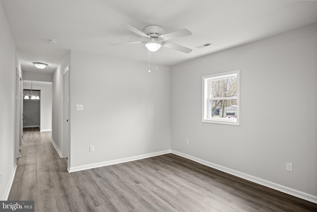 empty room featuring ceiling fan with notable chandelier and hardwood / wood-style floors