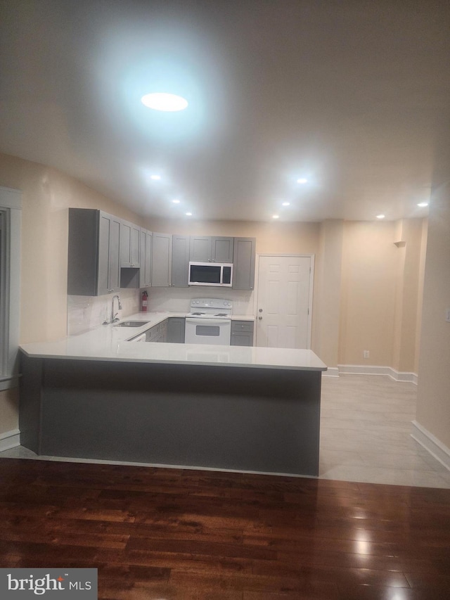 kitchen with kitchen peninsula, sink, hardwood / wood-style flooring, gray cabinets, and white range with electric cooktop