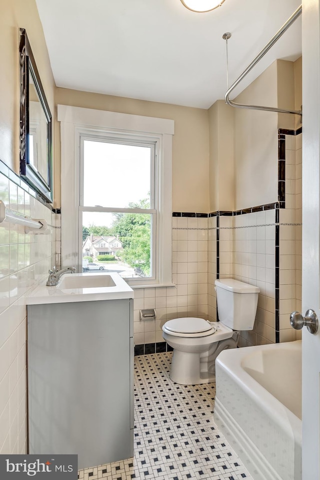 bathroom with a bathing tub, tile patterned floors, toilet, vanity, and tile walls