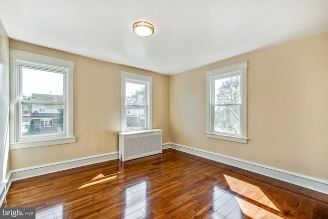 empty room featuring plenty of natural light, dark hardwood / wood-style floors, and radiator heating unit