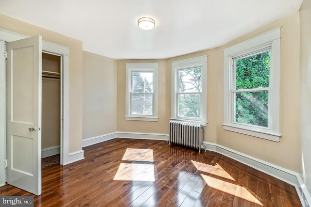 unfurnished bedroom featuring radiator heating unit, a closet, multiple windows, and dark wood-type flooring