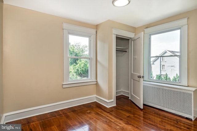 unfurnished bedroom featuring dark hardwood / wood-style floors, radiator heating unit, and a closet