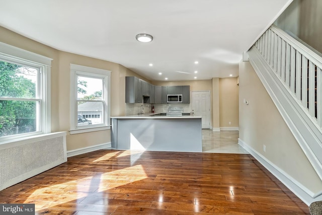 kitchen featuring radiator, white electric stove, wood-type flooring, gray cabinets, and decorative backsplash