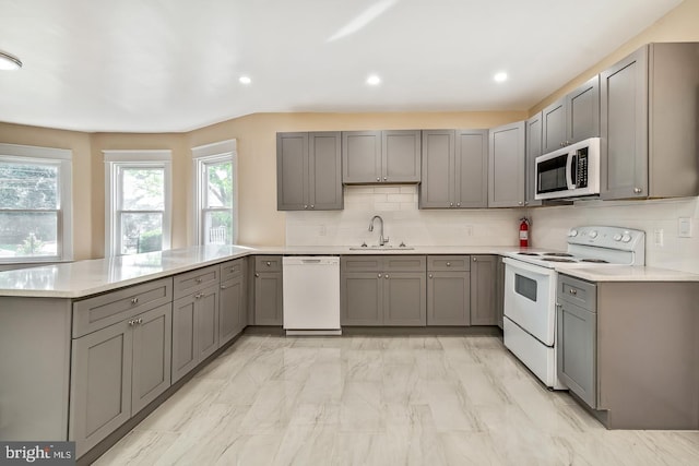 kitchen with backsplash, gray cabinetry, sink, and white appliances