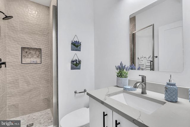 bathroom with a tile shower, vanity, and toilet