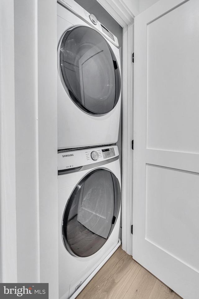 clothes washing area featuring light hardwood / wood-style floors and stacked washer and clothes dryer