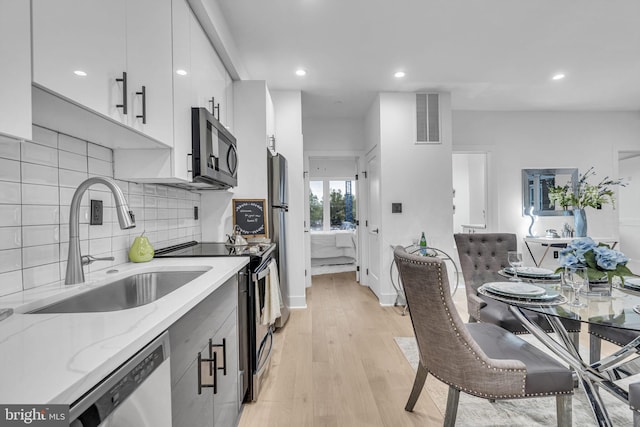 kitchen featuring white cabinets, sink, light wood-type flooring, light stone counters, and stainless steel appliances