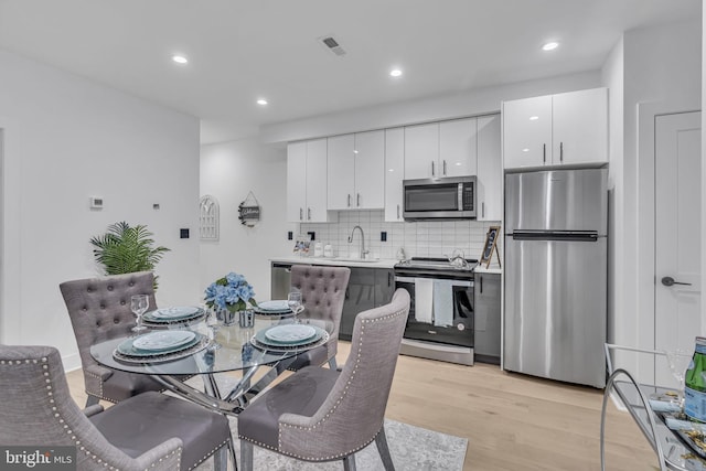 kitchen with white cabinets, sink, light hardwood / wood-style flooring, tasteful backsplash, and stainless steel appliances