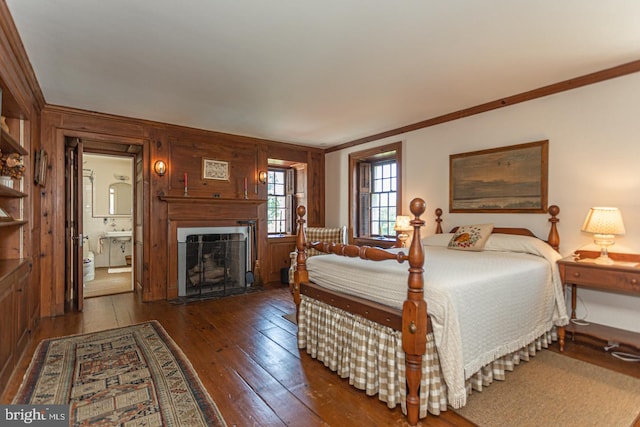 bedroom featuring dark hardwood / wood-style floors, wooden walls, crown molding, and connected bathroom