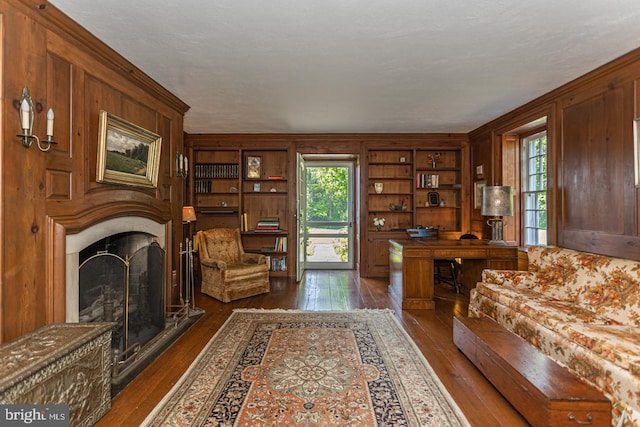 living room featuring dark wood-type flooring, built in shelves, and wood walls