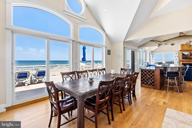 dining area featuring high vaulted ceiling, light hardwood / wood-style floors, a beach view, and a water view