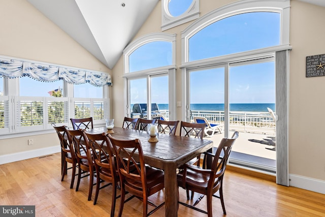 dining room featuring high vaulted ceiling, light hardwood / wood-style floors, and a water view