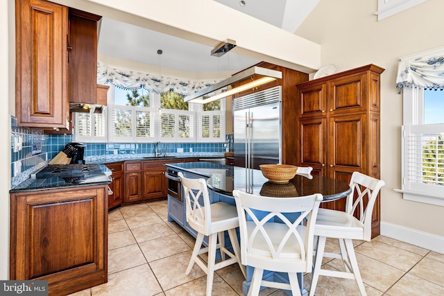 kitchen featuring stainless steel built in fridge, dark stone counters, backsplash, sink, and light tile flooring