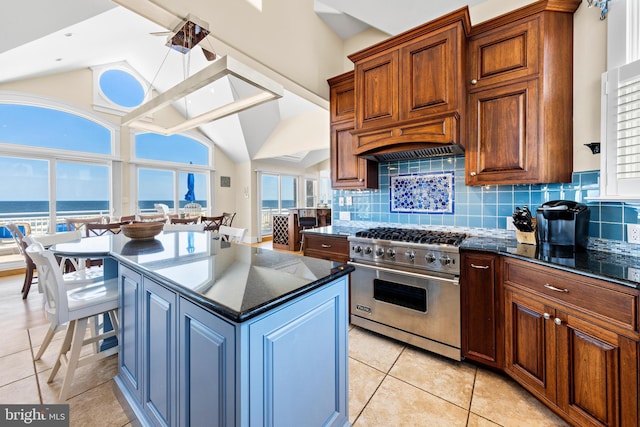 kitchen featuring dark stone counters, light tile flooring, tasteful backsplash, stainless steel range, and a center island