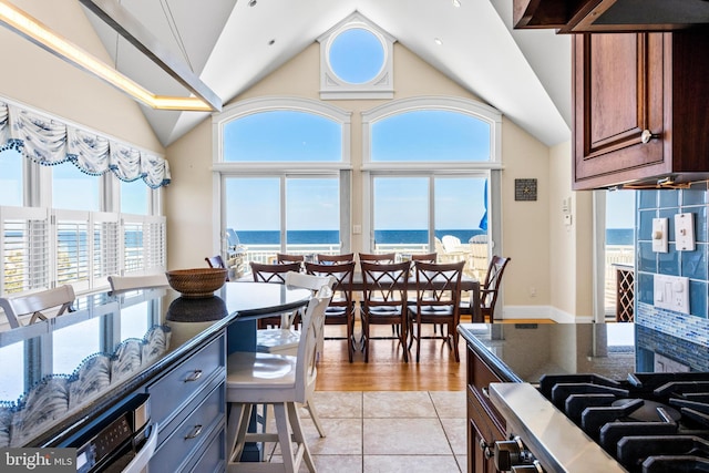 kitchen featuring a wealth of natural light, a water view, dark stone counters, and light tile flooring