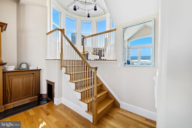 staircase featuring a raised ceiling, a healthy amount of sunlight, light hardwood / wood-style floors, and ornamental molding