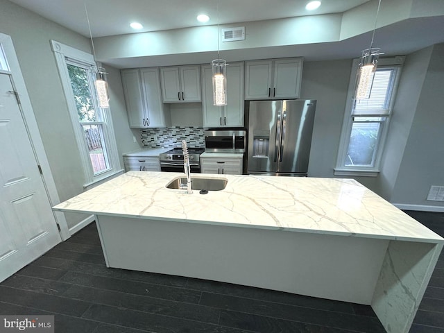 kitchen with gray cabinets, light stone counters, stainless steel appliances, and a kitchen island with sink