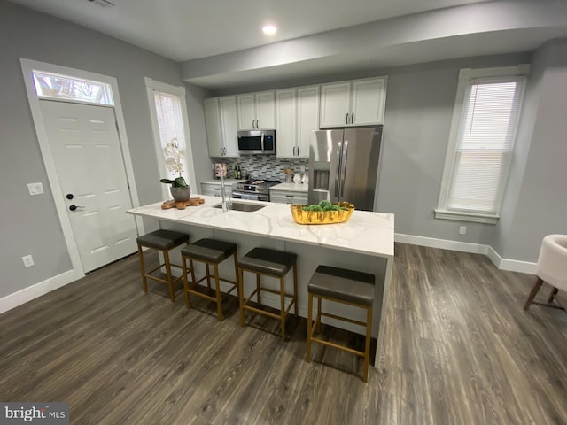 kitchen with light stone countertops, a kitchen breakfast bar, dark hardwood / wood-style flooring, a center island with sink, and appliances with stainless steel finishes