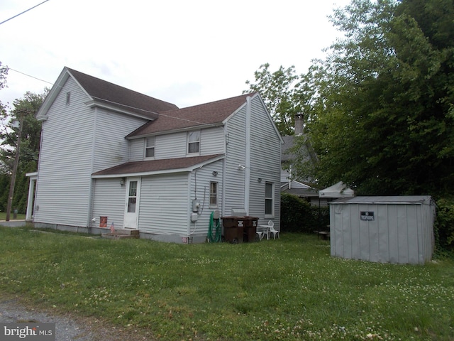 back of house with a lawn and a storage unit